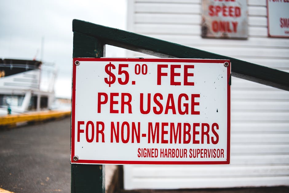A rectangular white sign with bold red text displaying a $5.00 fee per usage for non-members, attached to a dark green metal post with visible screws at each corner. The sign is positioned outdoors ne